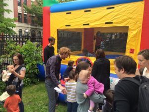 A group of kids and adults at a party outside, in front of a bouncy castle.